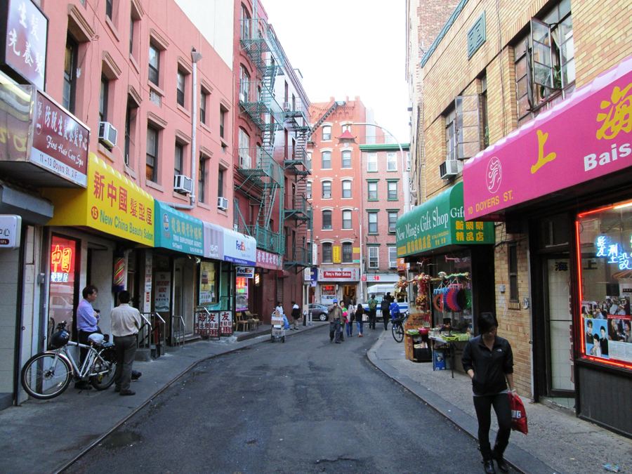The sharp bend of Doyers Street with lanterns, painted roadbed, and glowing storefronts