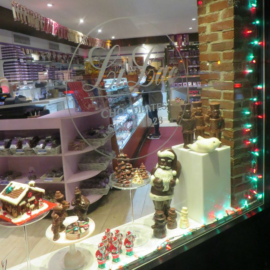 The holiday window of Li-Lac Chocolates in Greenwich Village, with the shop's etched logo on the glass and chocolate Santas on display