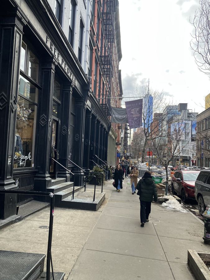 Shoppers on West Broadway in SoHo, with cast-iron storefronts and stoops along the sidewalk