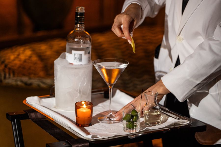 A bartender finishing a martini tableside at Hotel Chelsea's Lobby Bar, the gin on ice beside a candle