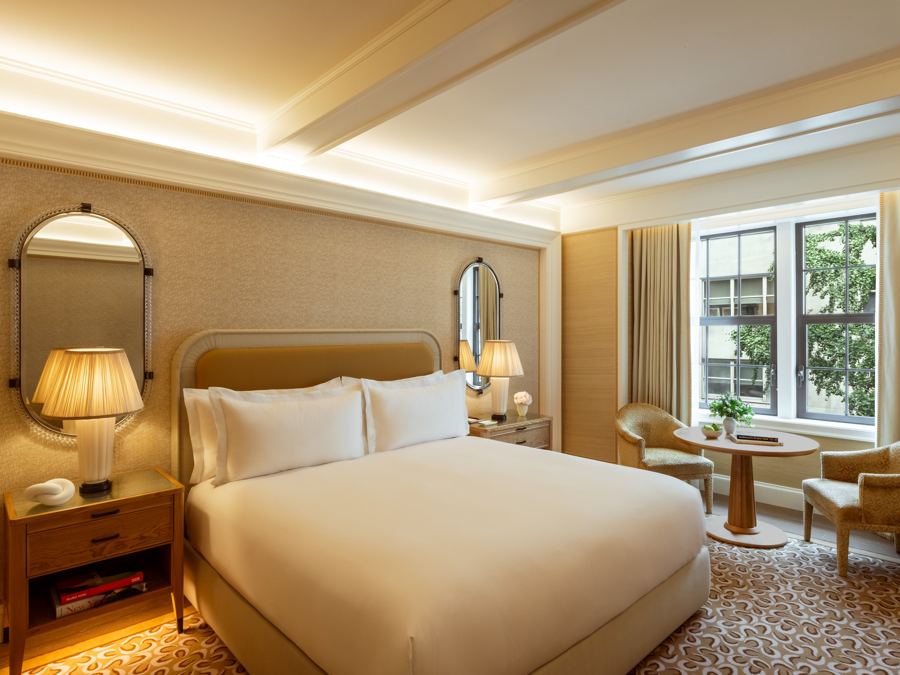 A Grand Deluxe King room with a cream bed, brass lamps and a reading table by the window