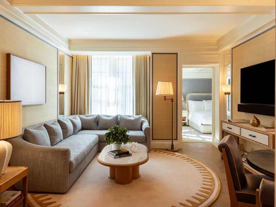 The living room of a Deluxe Suite, a soft gray sofa on a round rug, with the bedroom beyond