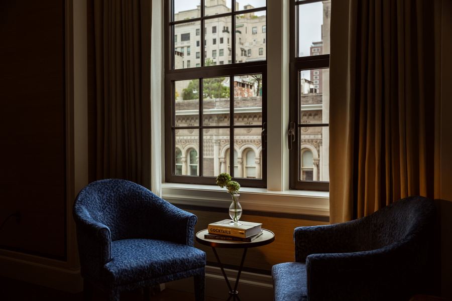 Two blue velvet armchairs by a tall window looking onto the Upper East Side