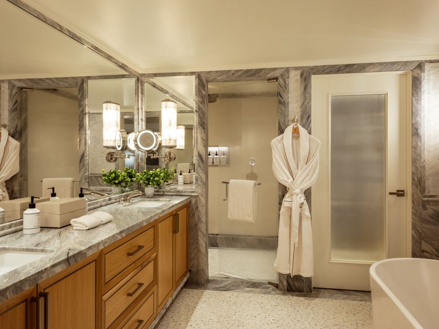 A marble bathroom with a double vanity, robes and a soaking tub