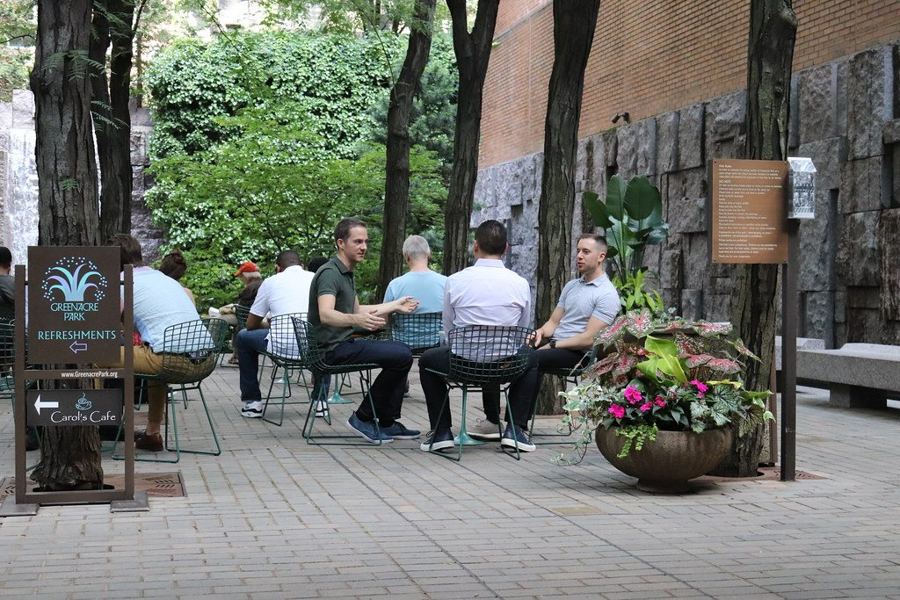 Visitors at tables in Greenacre Park, under honey locusts beside the stone waterfall wall