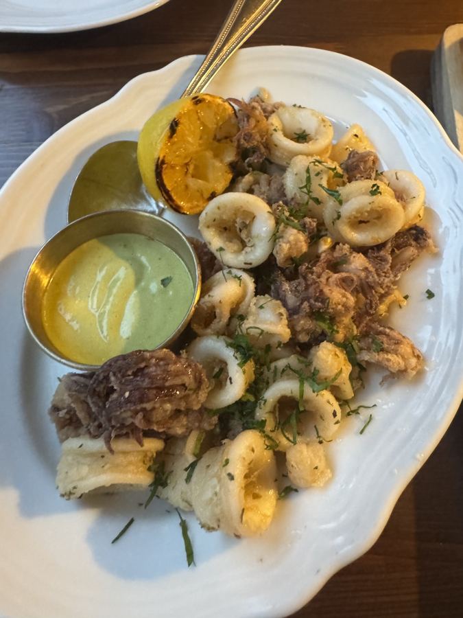 Fried calamari with a charred lemon half and a green-and-yellow dipping sauce on a white plate at Anémi in Astoria