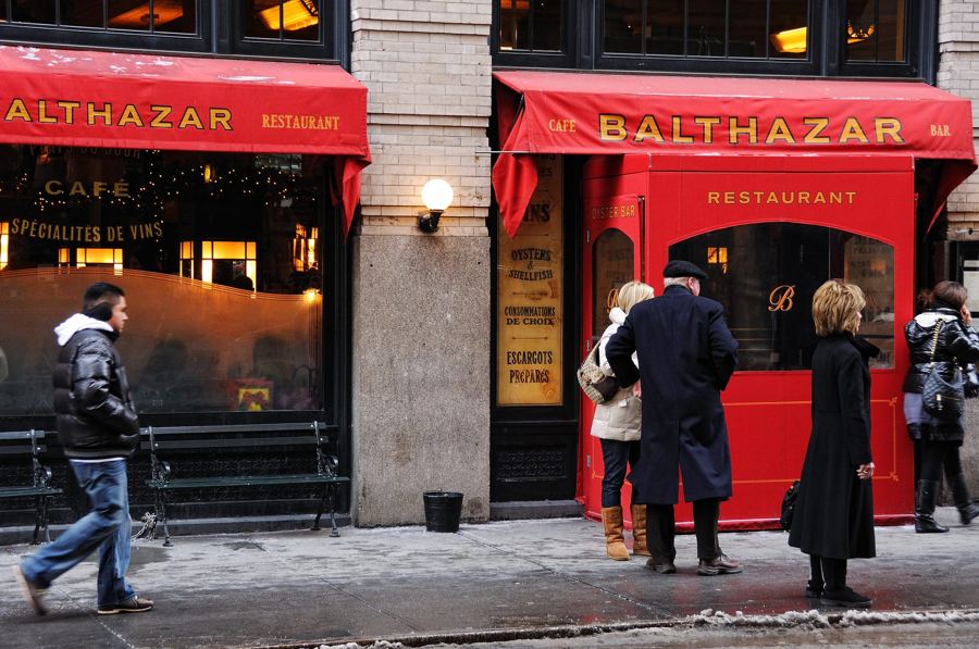 Pedestrians pass Balthazar's red 'Balthazar' awnings and red-framed doorway on a winter afternoon on Spring Street in SoHo.