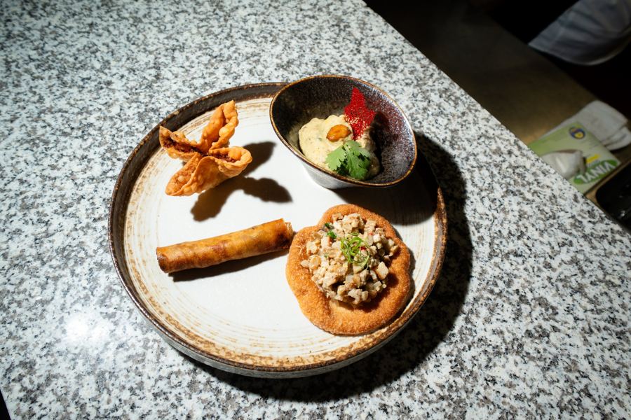 An appetizer plate of lumpia, crisp wontons and a small tostada with dip on a granite counter