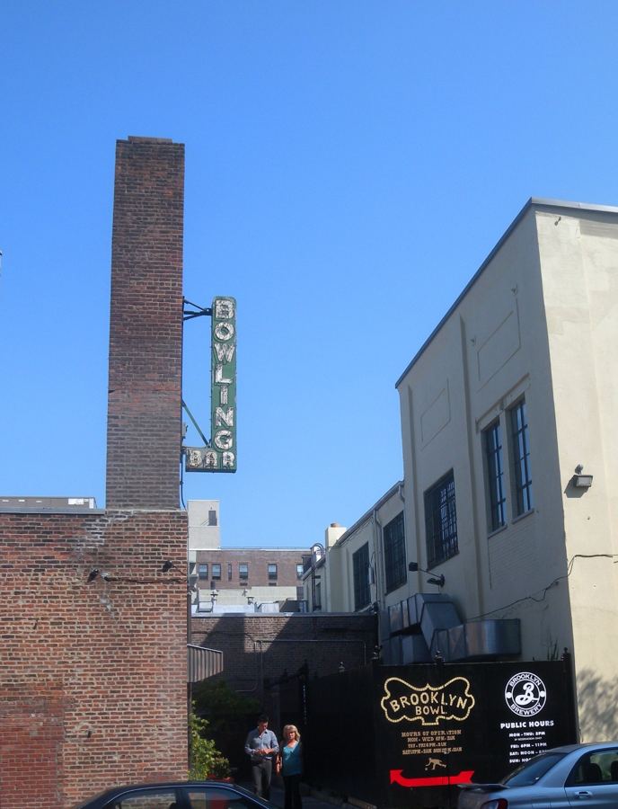 Brooklyn Bowl's brick chimney with its vertical 'Bowling Bar' sign and the venue's entrance signage on Wythe Avenue in Williamsburg