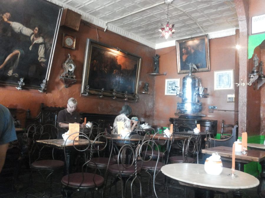 The dim, old-world interior of Caffè Reggio with Renaissance-style oil paintings on terracotta walls, a brass espresso machine and marble café tables.