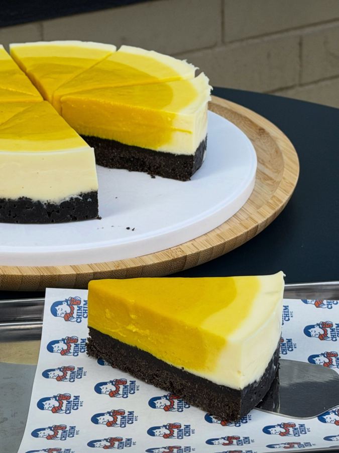 A yellow-topped cheesecake on a dark cookie crust, sliced on a board at Chim Chim