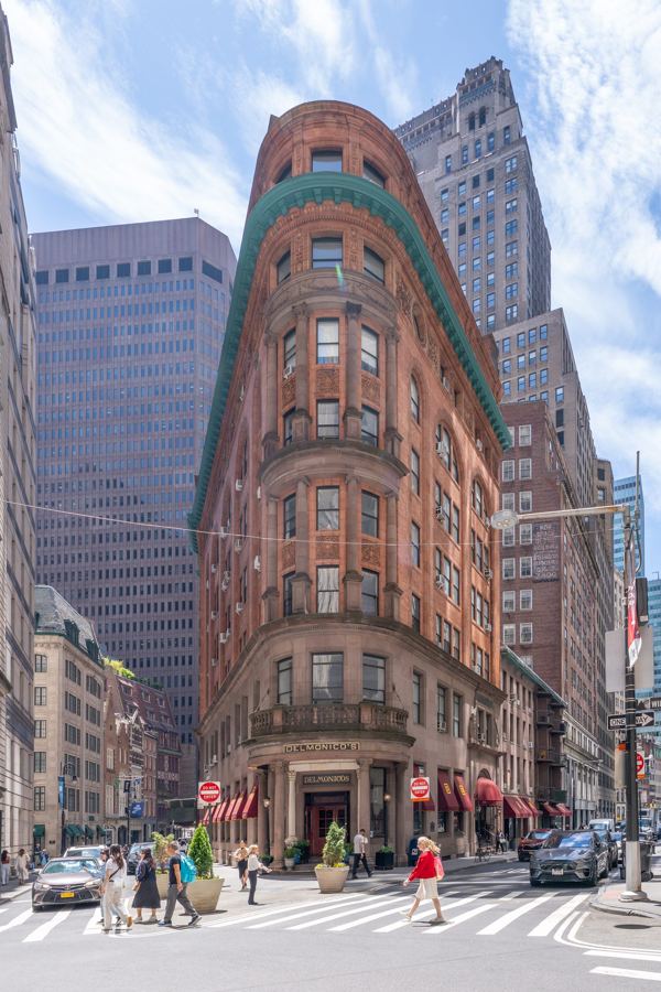 The rounded, wedge-shaped brick Delmonico's Building rises at the corner of Beaver and South William Streets, with the restaurant's portico at street level.