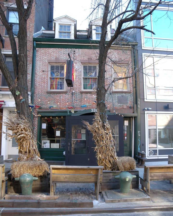 The narrow Federal-style brick front of the Ear Inn on Spring Street, with its dark green bar windows, wooden benches and bollards on the sidewalk.