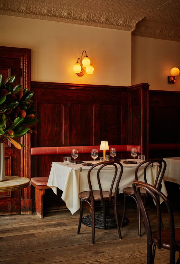 A corner banquette set for dinner beneath brass sconces