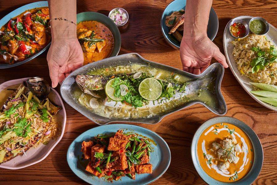 A Thai spread at Fish Cheeks in Williamsburg — a whole steamed fish with lime and herbs on a fish-shaped platter, coconut crab curry and more shared plates on a wooden table