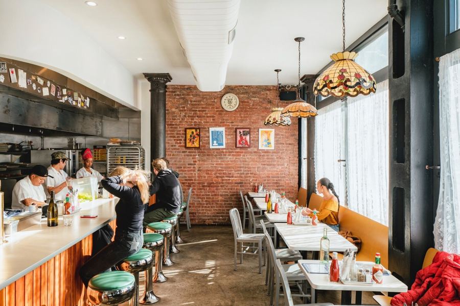 Golden Diner's sunny dining room, with a long counter and green stools, a brick wall and stained-glass pendant lamps