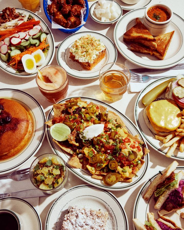 A table spread at Golden Diner: pancakes, nachos, salad, wings, a club sandwich and a burger with fries