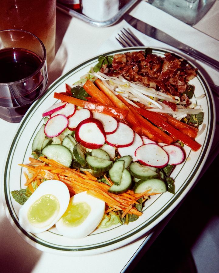 A chopped salad with radishes, cucumber, carrot, peppers, halved eggs and meat on an oval Golden Diner platter