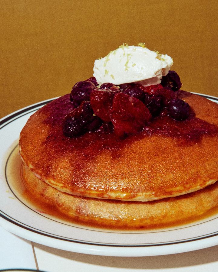 A tall stack of Golden Diner's honey butter pancakes topped with berry compote and whipped butter, syrup pooling on a green-rimmed plate