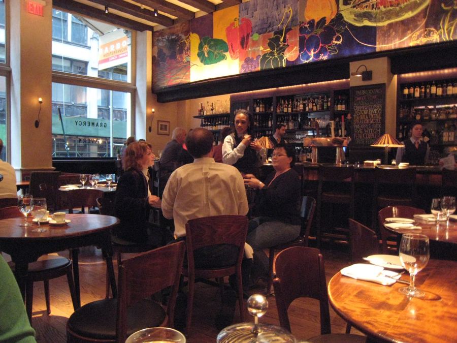 Diners at round wooden tables in Gramercy Tavern's warmly lit front room, beneath a painted fruit-and-vegetable mural and the back bar.