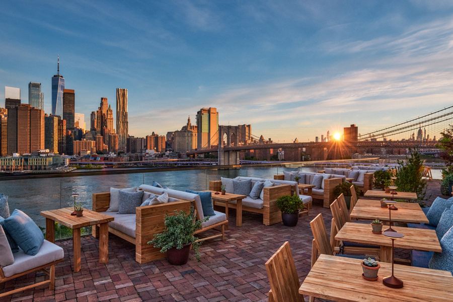 Harriet's Rooftop terrace at sunset, with sofas and low tables facing the Lower Manhattan skyline across the East River