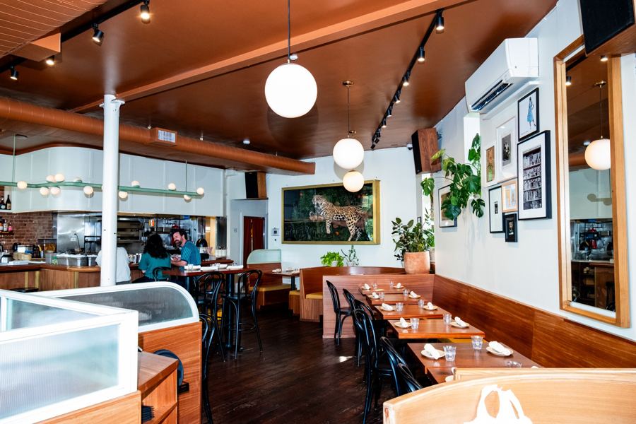 The dining room at Hellbender in Ridgewood — globe pendant lights, wood banquettes and a large jaguar painting on the back wall