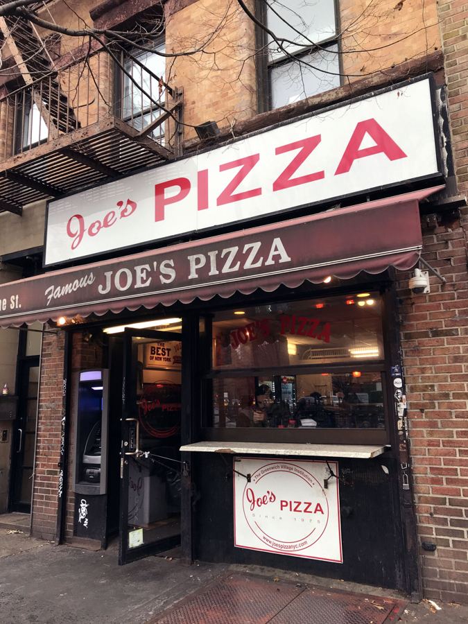 The red-and-white 'Joe's Pizza' sign and maroon 'Famous Joe's Pizza' awning over the slice counter at 7 Carmine Street in Greenwich Village