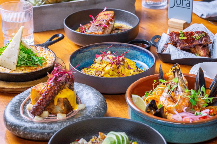 A table spread of Peruvian dishes at Jora in Long Island City: rice, octopus, mussels, ribs and a skillet under a Jora menu card