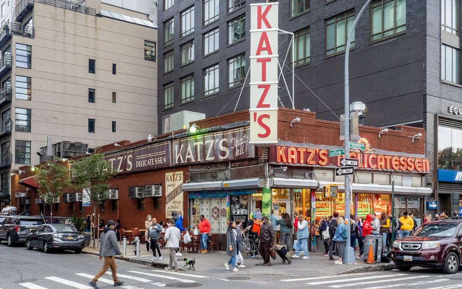 Katz's Delicatessen at the corner of Houston and Ludlow Streets, with its vertical 'Katz's' sign and red neon 'Katz's Delicatessen' lettering above a busy sidewalk