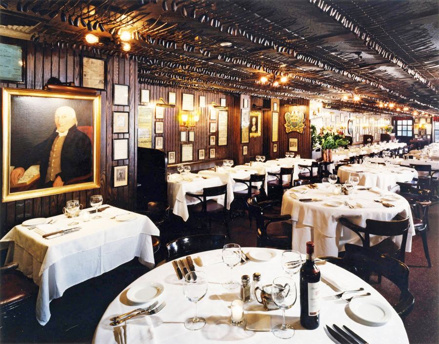 The dining room at Keens Steakhouse: white tablecloths, dark wood, an oil portrait and thousands of clay pipes along the ceiling