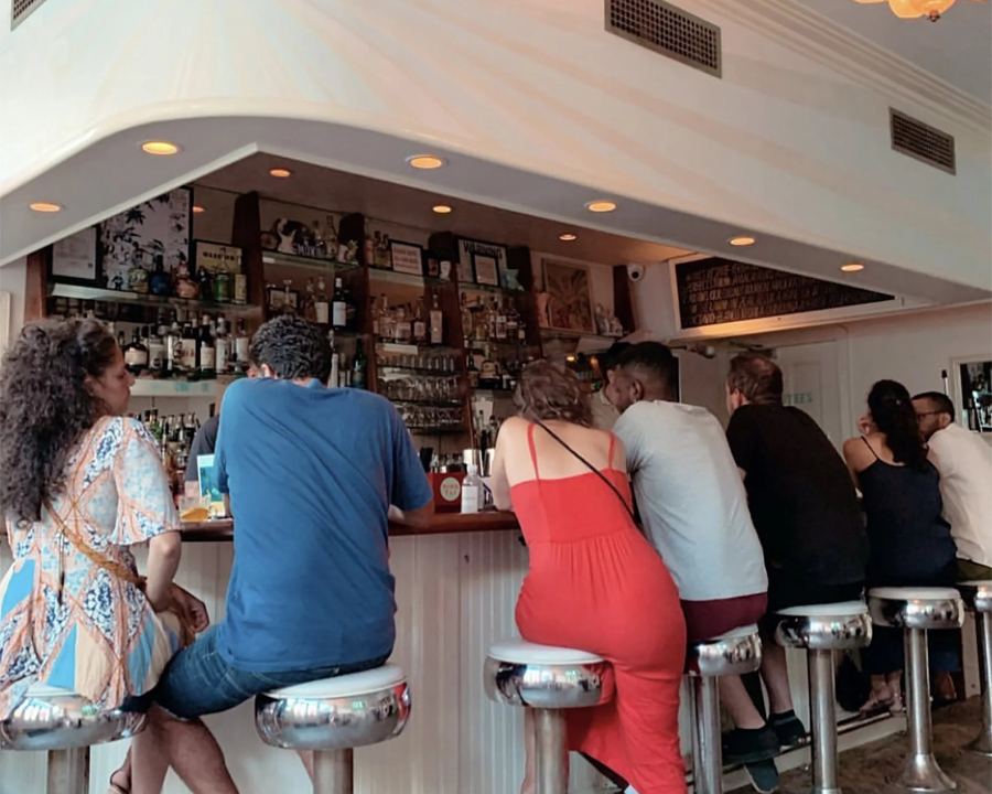 Guests on chrome stools at the curved bar at King Tai in Crown Heights, under a white-painted ceiling with the back bar lit up