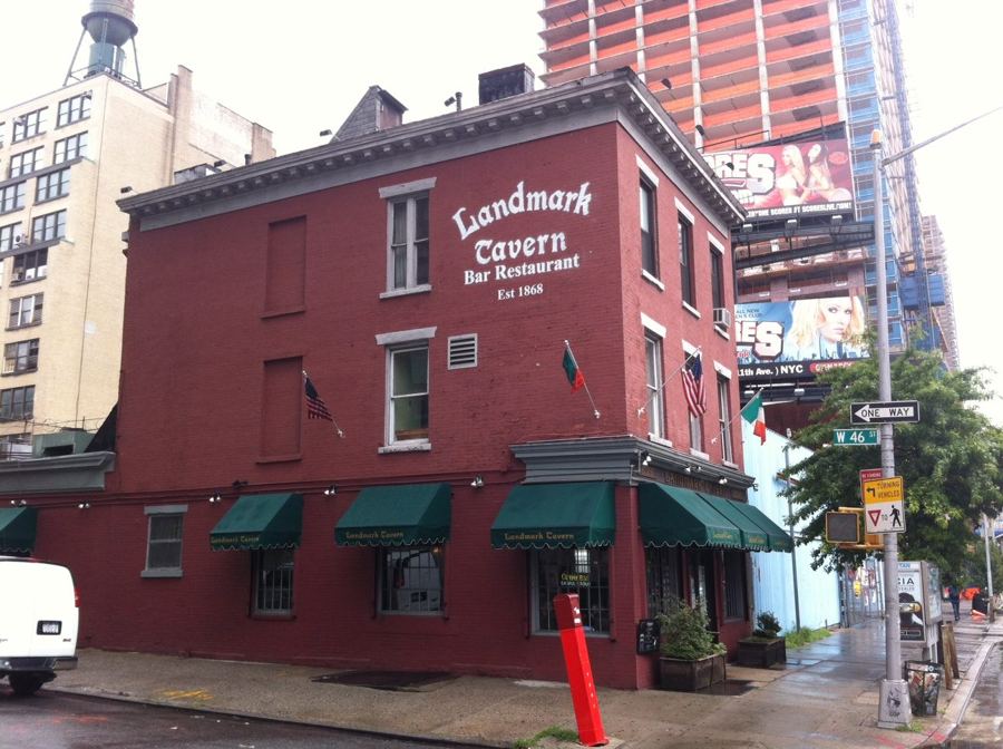 The three-story red-brick Landmark Tavern on 11th Avenue, with its painted 'Landmark Tavern Bar Restaurant Est. 1868' sign and green awnings over the ground-floor windows.