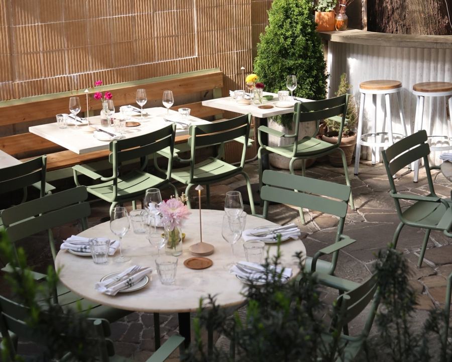 Set tables, green chairs and potted evergreens on the stone-paved back patio at LaRina in Fort Greene