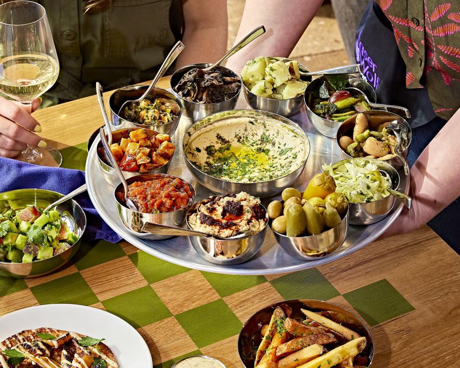 The salatim tray at Laser Wolf Brooklyn: hummus, pickles, olives and a ring of small salads, with fries and a glass of white wine