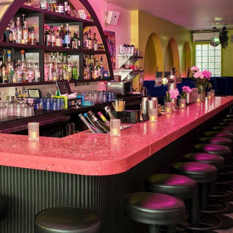 The pink terrazzo bar at Lise & Vito in Greenpoint, with stools and backlit bottle shelves under an arch