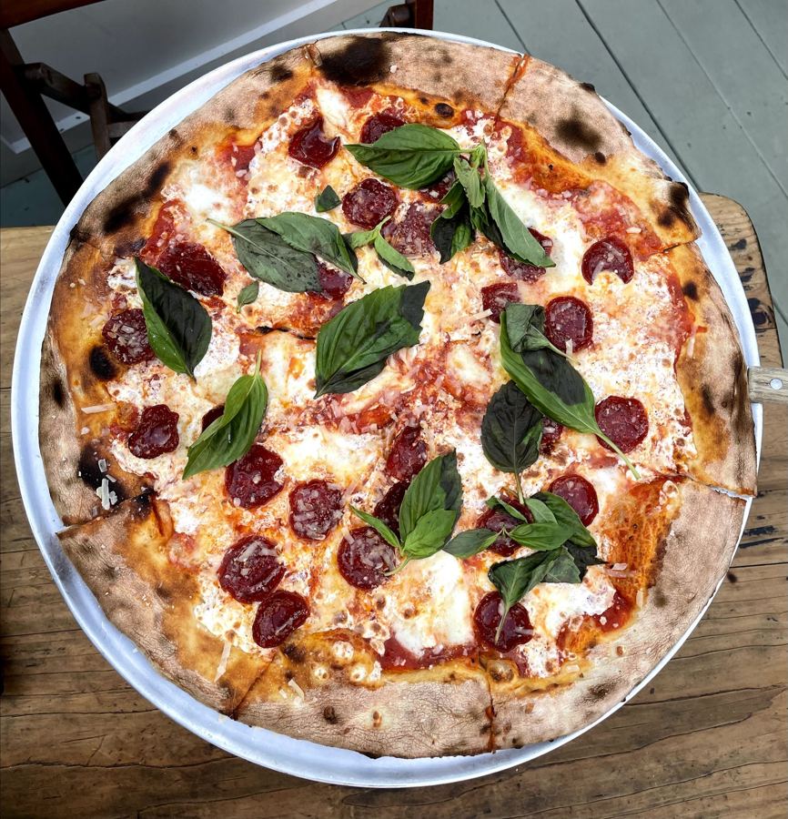 Overhead view of a blistered Lucali pizza topped with pepperoni, fresh mozzarella and torn basil on a metal tray.