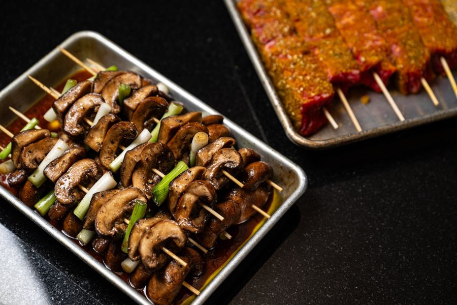 Trays of mushroom and scallion skewers and marinated beef skewers ready for the grill at Messy