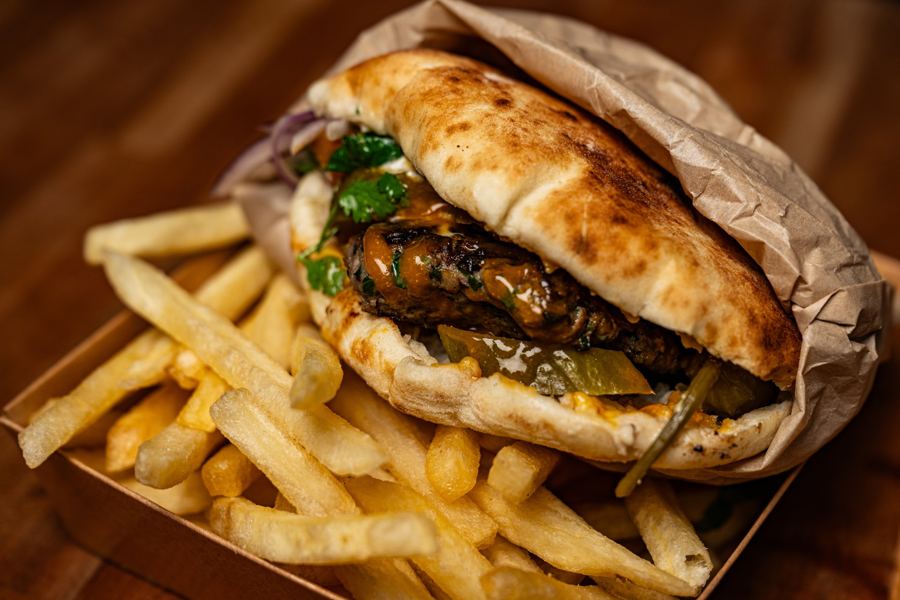 A pita stuffed with grilled skewer meat and herbs beside a pile of fries