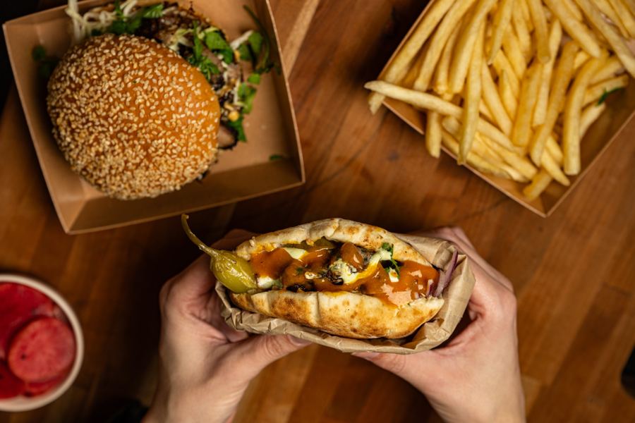 Hands holding a stuffed pita over a table of burgers, fries and pickled beets at Messy