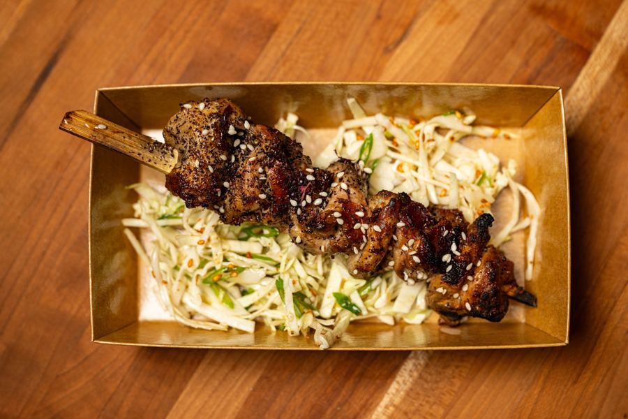 A glazed steak skewer laid over shredded cabbage slaw in a kraft box at Messy