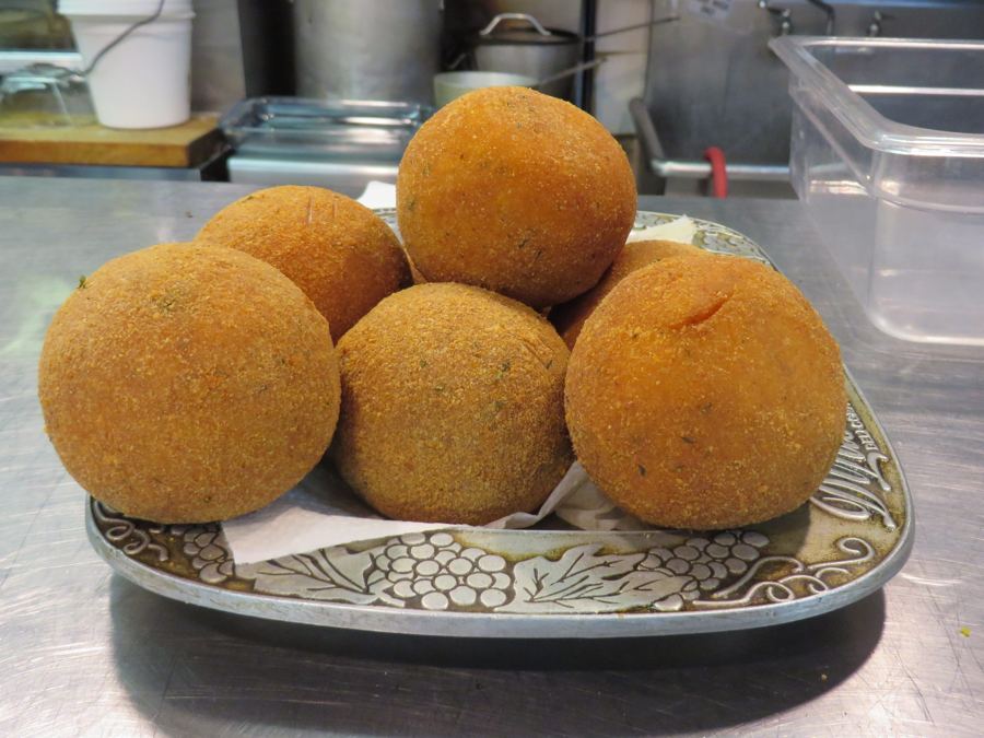 Five golden fried arancini rice balls on an embossed metal platter in the kitchen at Mike's Deli on Arthur Avenue.