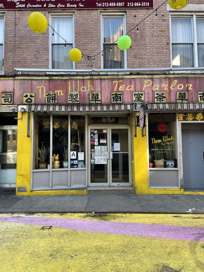 The yellow-trimmed storefront of Nom Wah Tea Parlor on Doyers Street, with its vintage red sign in English and Chinese and paper lanterns overhead.