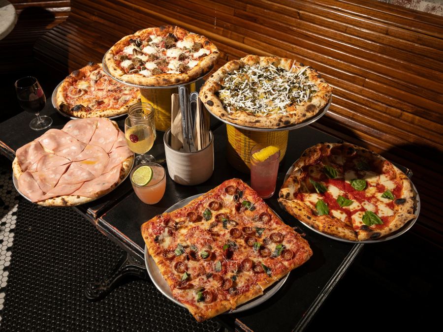 Square pepperoni and round sourdough pizzas, mortadella and drinks spread across a dark table at Ops in Bushwick