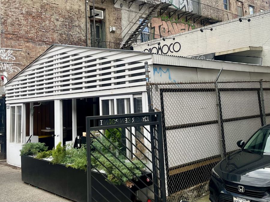 Oxomoco's white slatted pavilion-style front on Greenpoint Avenue, with its script sign on the wall above and planters by the gate.