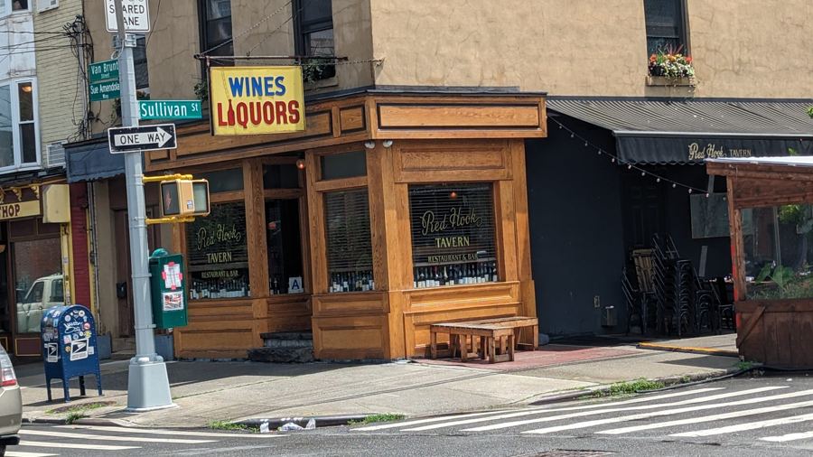 The warm wood-paneled corner storefront of Red Hook Tavern on Van Brunt Street, with gold-lettered windows and a bench out front.