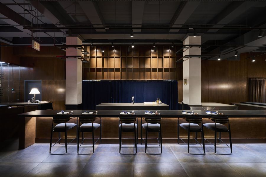 Black counter stools facing the long open kitchen at Restaurant Yuu, under dark wood shelving and spotlights