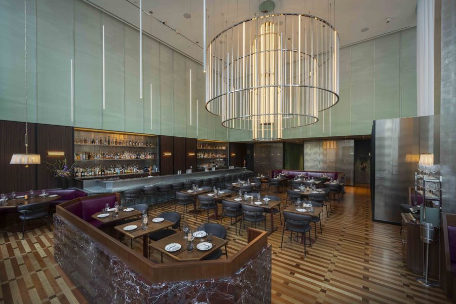 Saverne's dining room in Hudson Yards, with a tall ring chandelier, green walls and a long bar