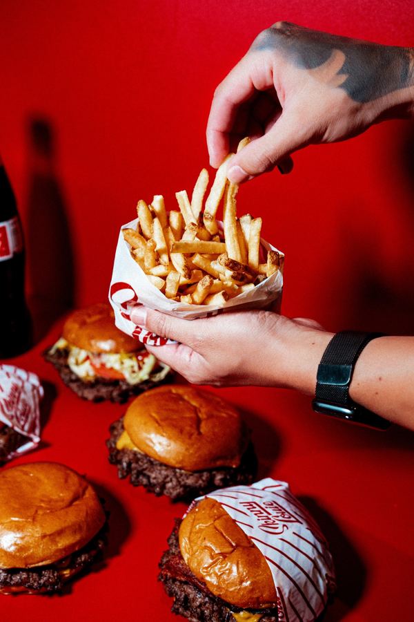 Fries and smash burgers on a red table at Skinny Louie