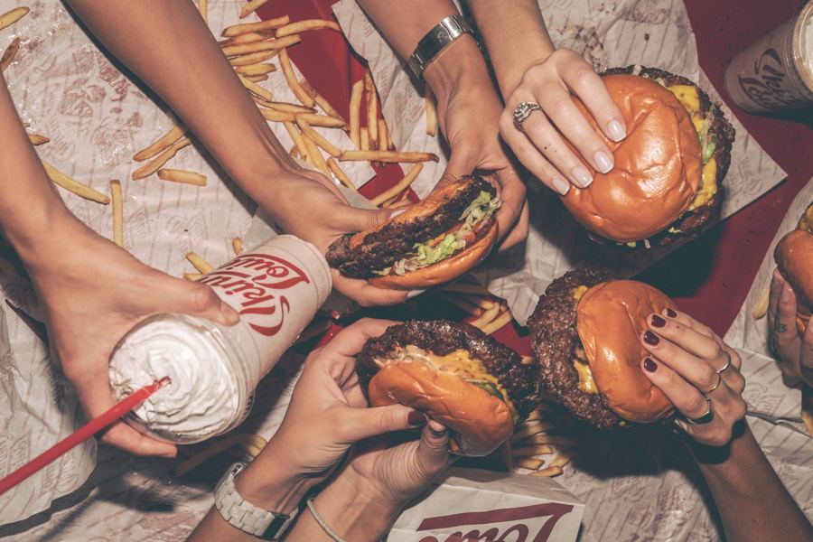 Hands reaching for smash burgers, fries and milkshakes in Skinny Louie's striped wrappers