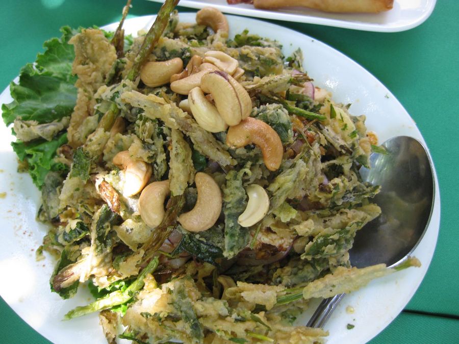 A plate of SriPraPhai's crispy fried green salad tossed with cashews and seafood on a green tablecloth.